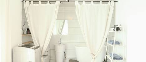 Un baño con lavadora, inodoro y repisas con ropa doblada.