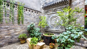 Une cour bordée de murs en briques, agrémentée de plantes en pot et d’un panneau décoratif en pierre.