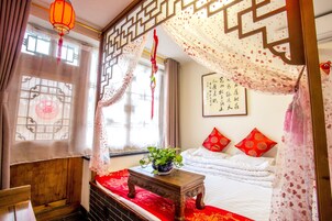 Una habitación tradicional con una cama, una mesita con una planta, un adorno en la pared y una ventana con cortinas.