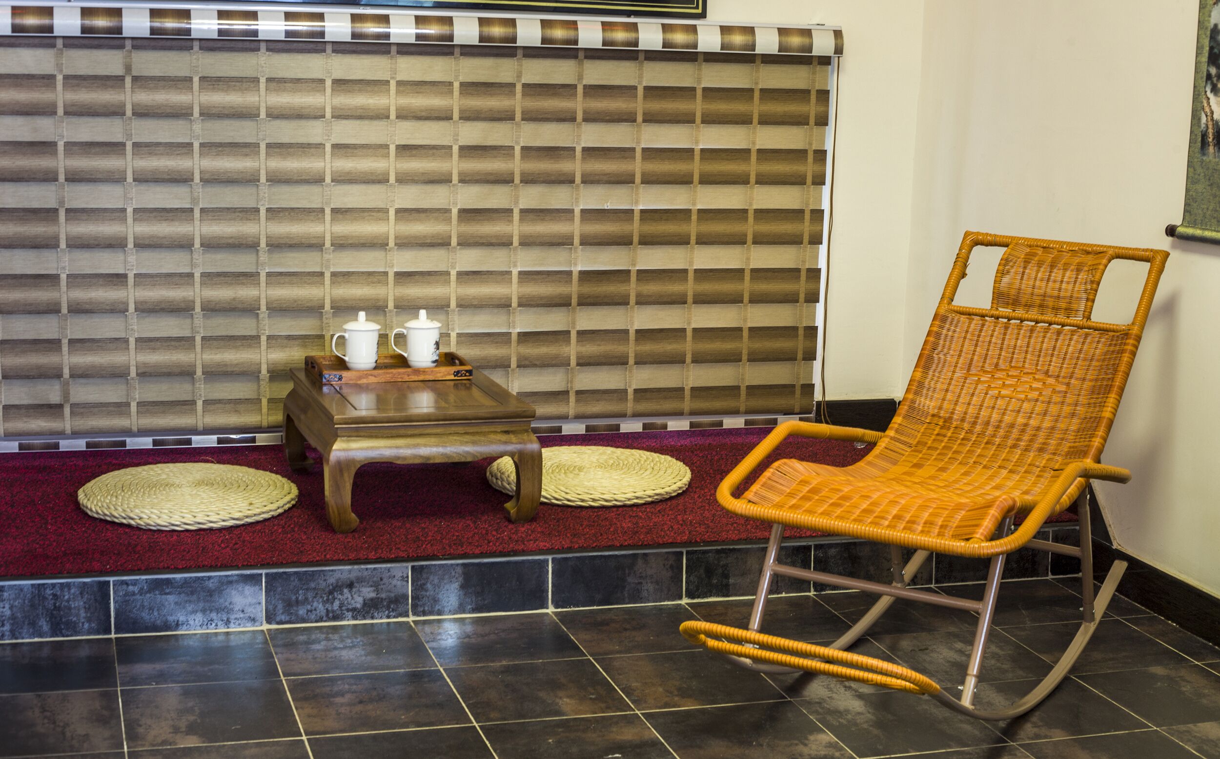 A room with a wicker rocking chair, a small wooden table with two white cups, and a checkered floor.