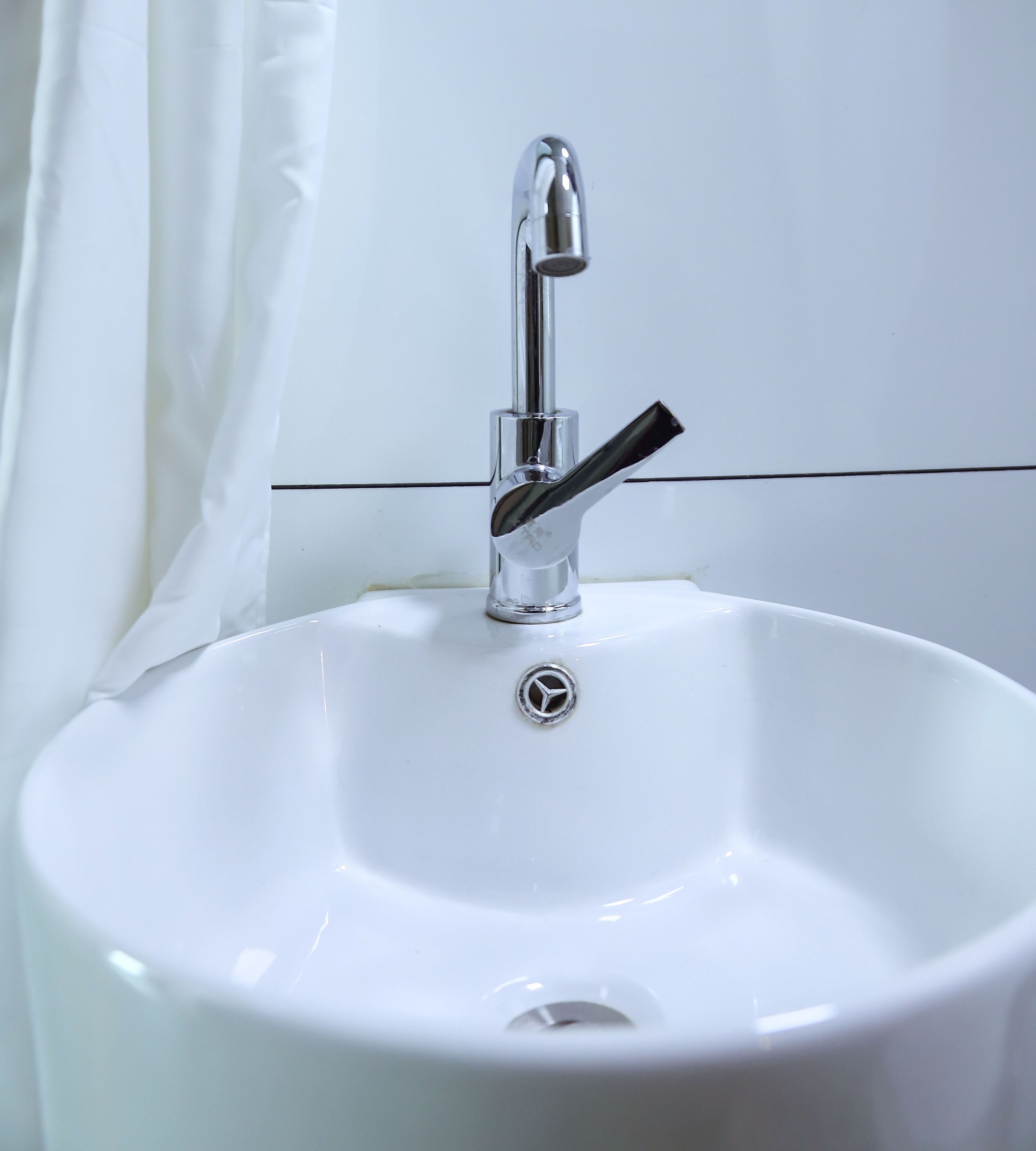 Ein weißes Waschbecken mit chromfarbenem Wasserhahn und einem Abfluss.