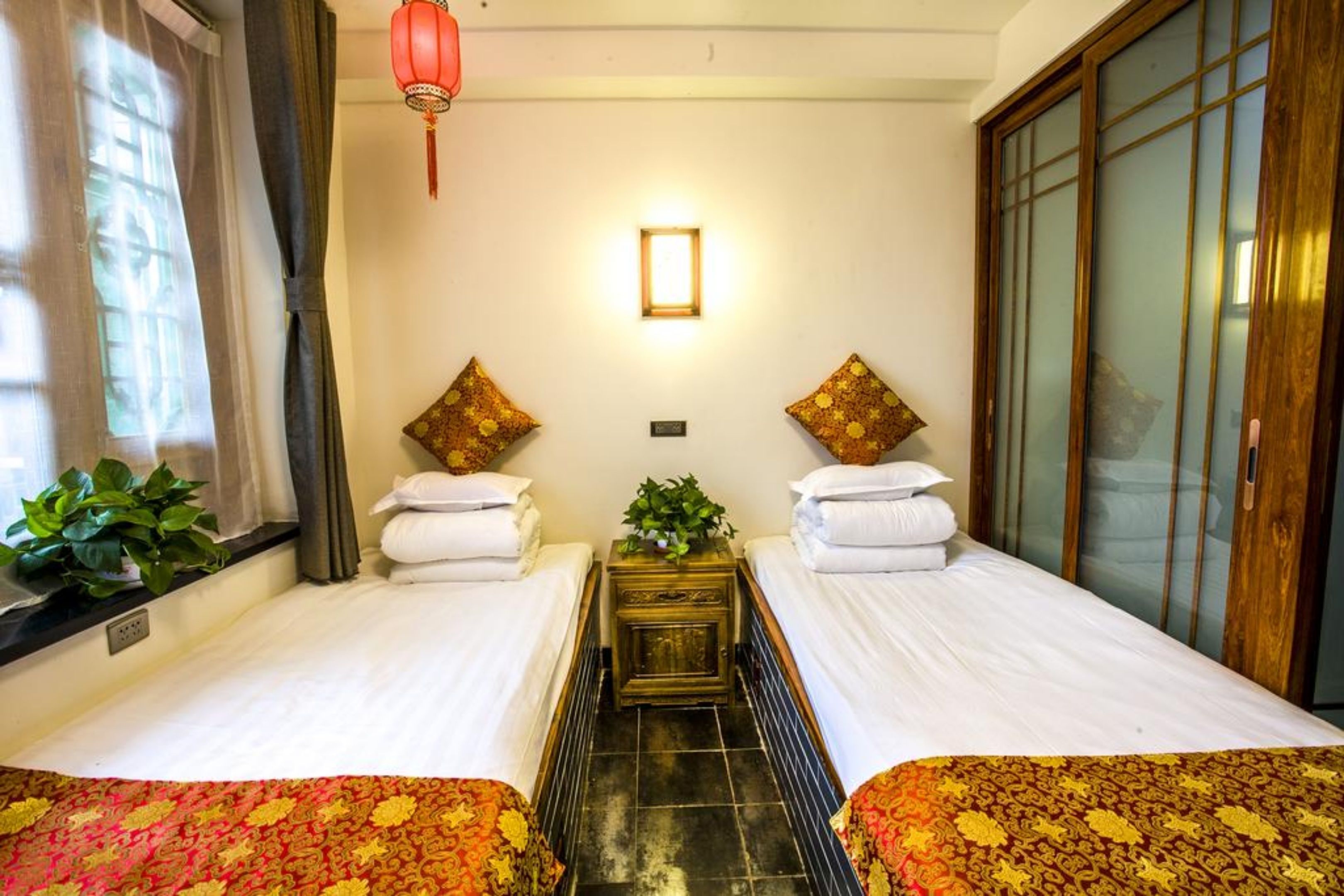 A hotel room with two beds, a small table with a plant, a red lantern, and a sliding door.