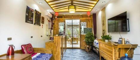 A traditional-style room with a wooden ceiling, a sofa, a table, a TV, and a large water dispenser.