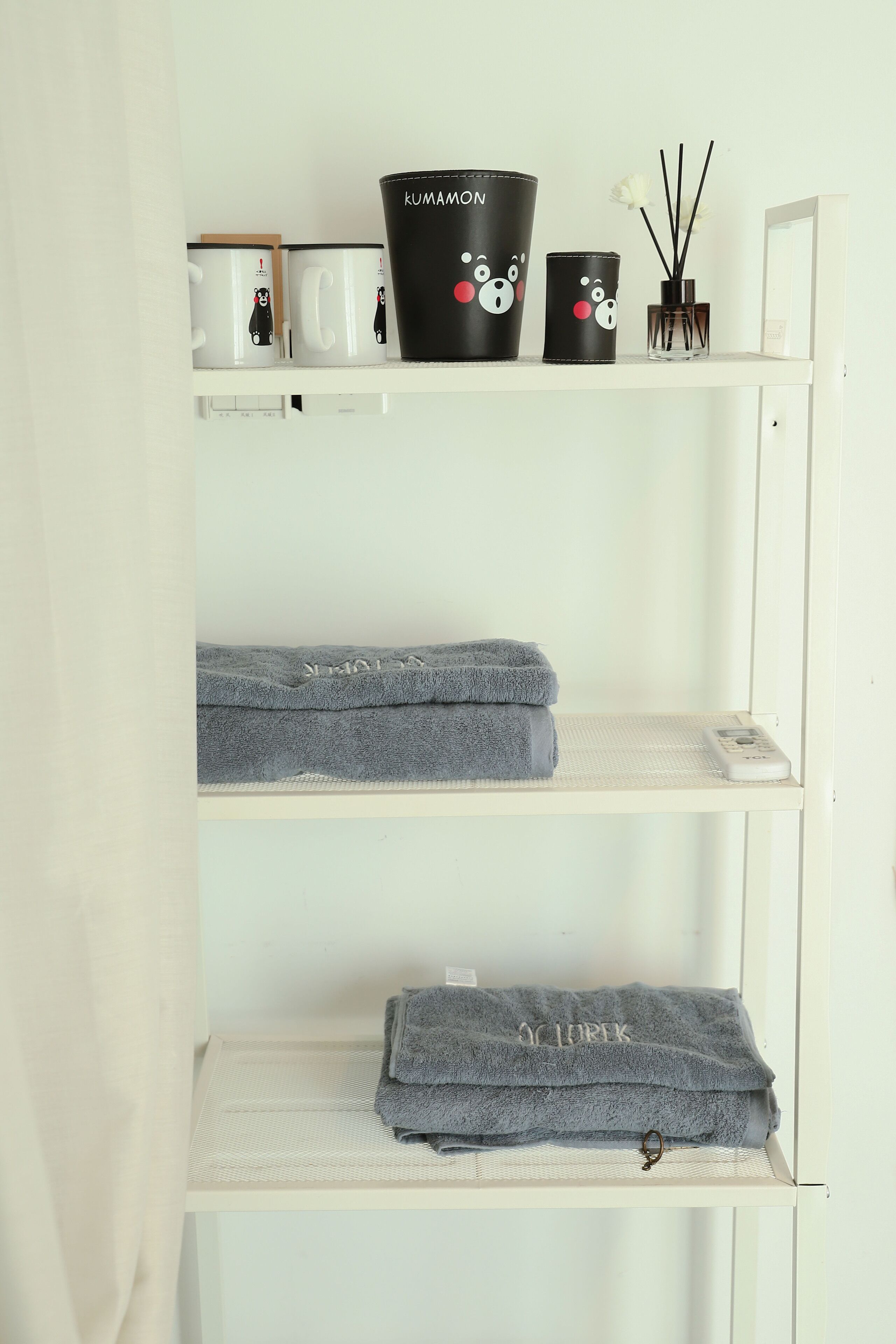 A white shelf with three grey towels, a black mug with a bear design, and a black container with a bear design.
