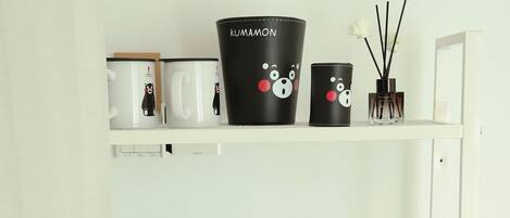 A white shelf with three grey towels, a black mug with a bear design, and a black container with a bear design.