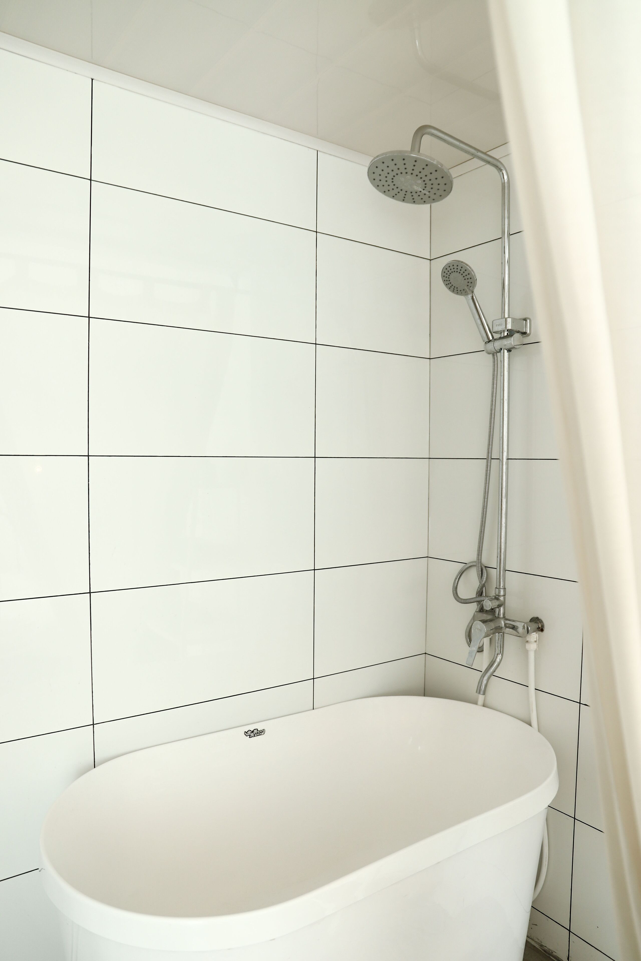 A modern bathroom with white tiles, a freestanding bathtub, and a shower with a handheld showerhead.