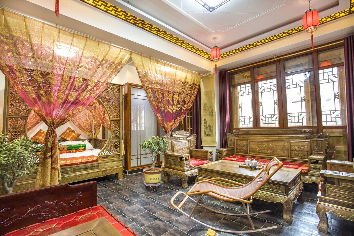 A traditional room with a bed, a rocking chair, a table, and a window with curtains.
