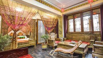 Una habitación tradicional con una cama, un sillón mecedora, una mesa y un ventanal con cortinas.