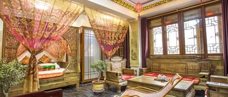 A traditional room with a bed, a rocking chair, a table, and a window with curtains.