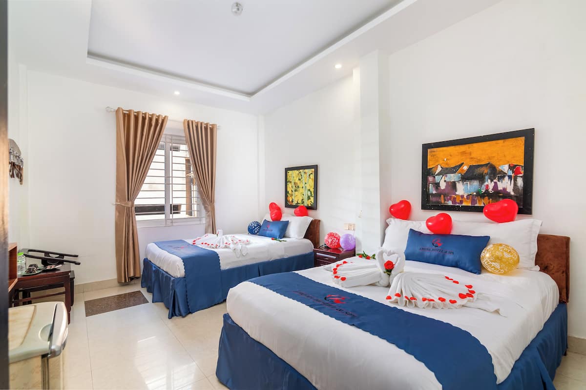 A hotel room with two beds, a desk, and a window with curtains.