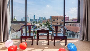 A balcony with a table and chairs, overlooking a cityscape with buildings and a clear sky. - Amona Hotel - Hostel (Hue)