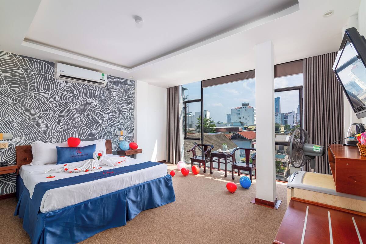 A modern hotel room with a large bed, a desk, and a balcony with a city view.