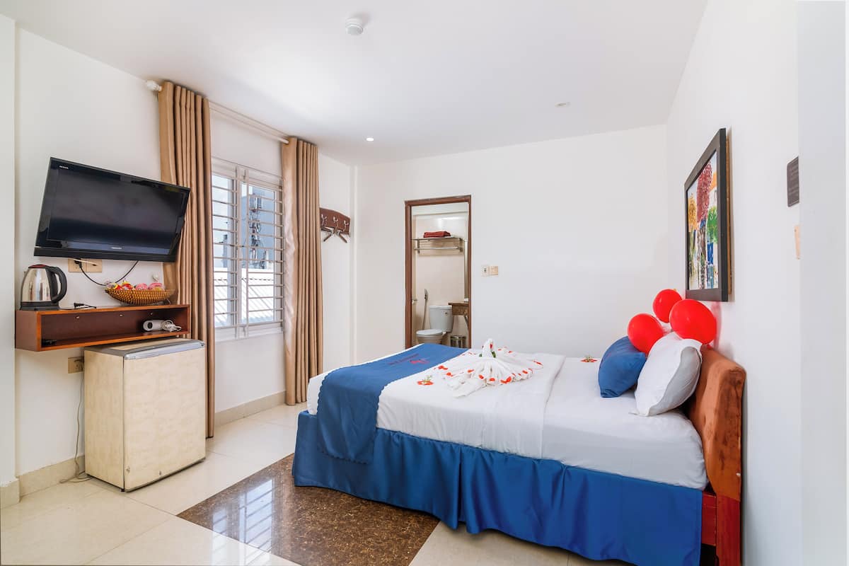 A hotel room with a bed, a television, a small refrigerator, and a window with curtains.