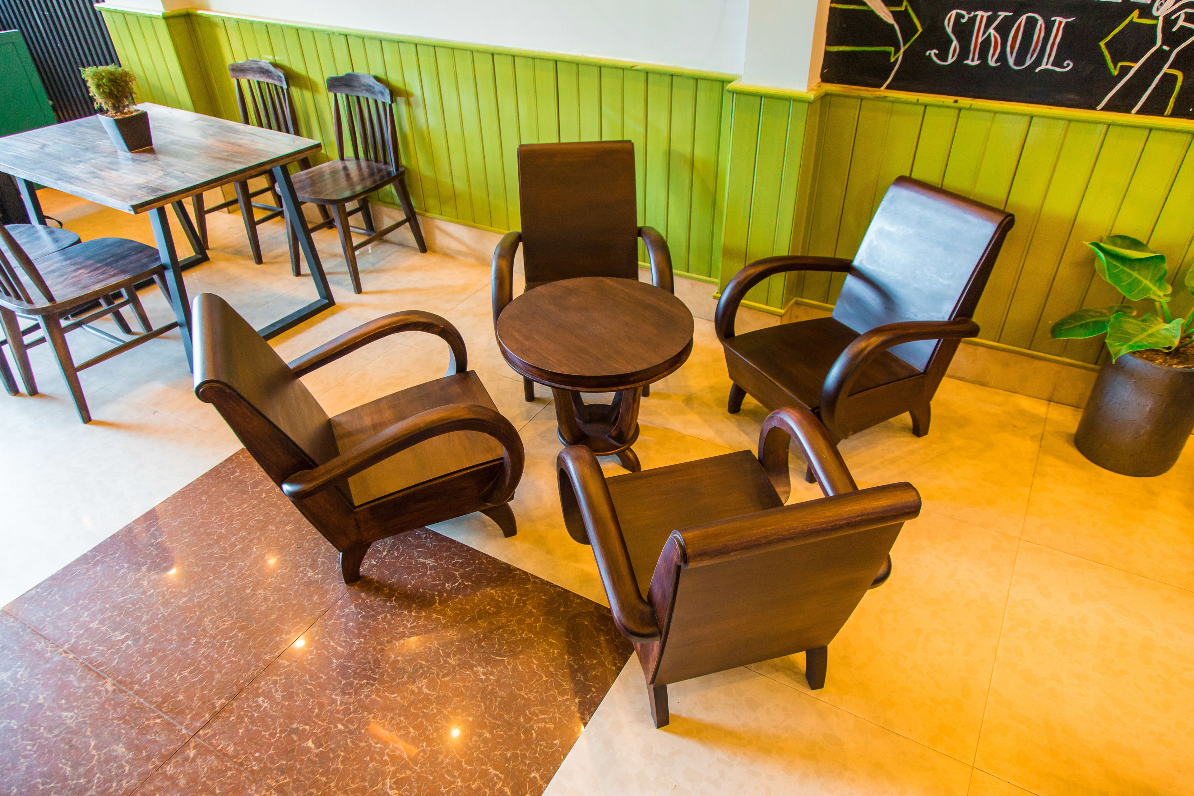 A restaurant interior with a green and white color scheme, featuring a wooden table and chairs, a potted plant, and a chalkboard sign.