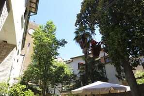 A narrow street with buildings, trees, and a white umbrella. - Hotel Posta (Orvieto)