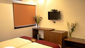 A hotel room with two beds, a desk, a TV, and a window with a blind.