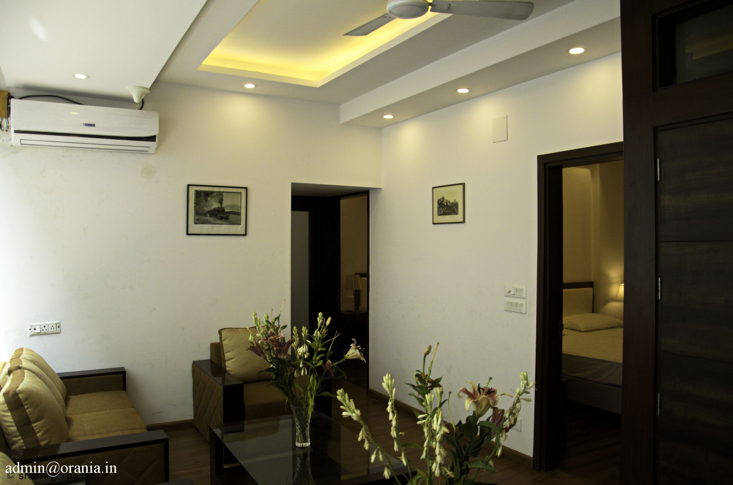 A hotel lobby with a sofa, a table with flowers, a ceiling fan, and an air conditioning unit.