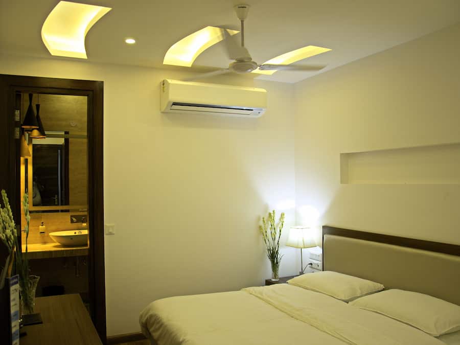 Habitación de hotel con cama, lámpara de noche, aire acondicionado y ventilador de techo, además de un espejo en una esquina.
