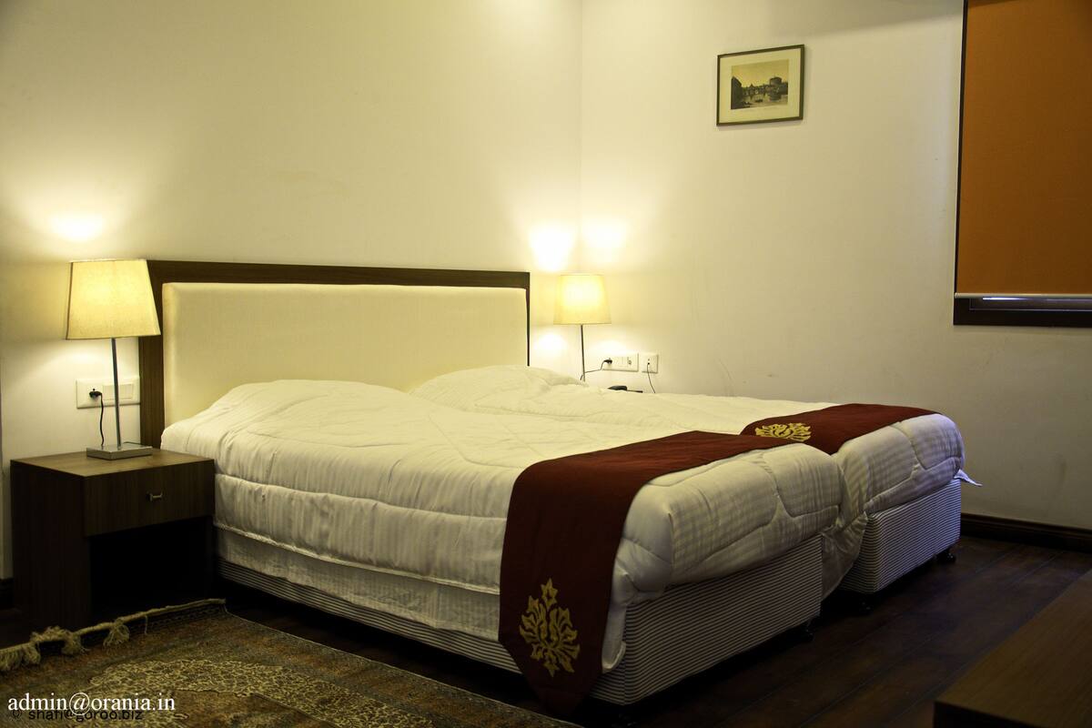Una cama doble bien hecha con cabecera blanca, dos lámparas de noche y una mesita de noche pequeña.