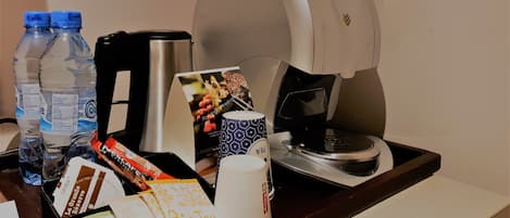 A hotel room's breakfast area with a coffee maker, water bottles, a mug, and some breakfast items on a tray.