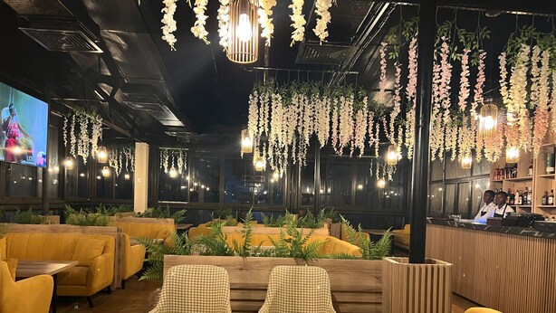 A restaurant with yellow seating, hanging floral decorations, and a bar area. - Grand Hotel Central (Conakry)