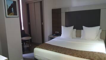 A hotel room with a large bed, a bedside table with a phone and scissors, a chair, and a painting on the wall.