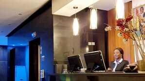 A modern reception desk with a receptionist, a computer, and a vase with flowers. - Grand Hotel Central (Conakry)