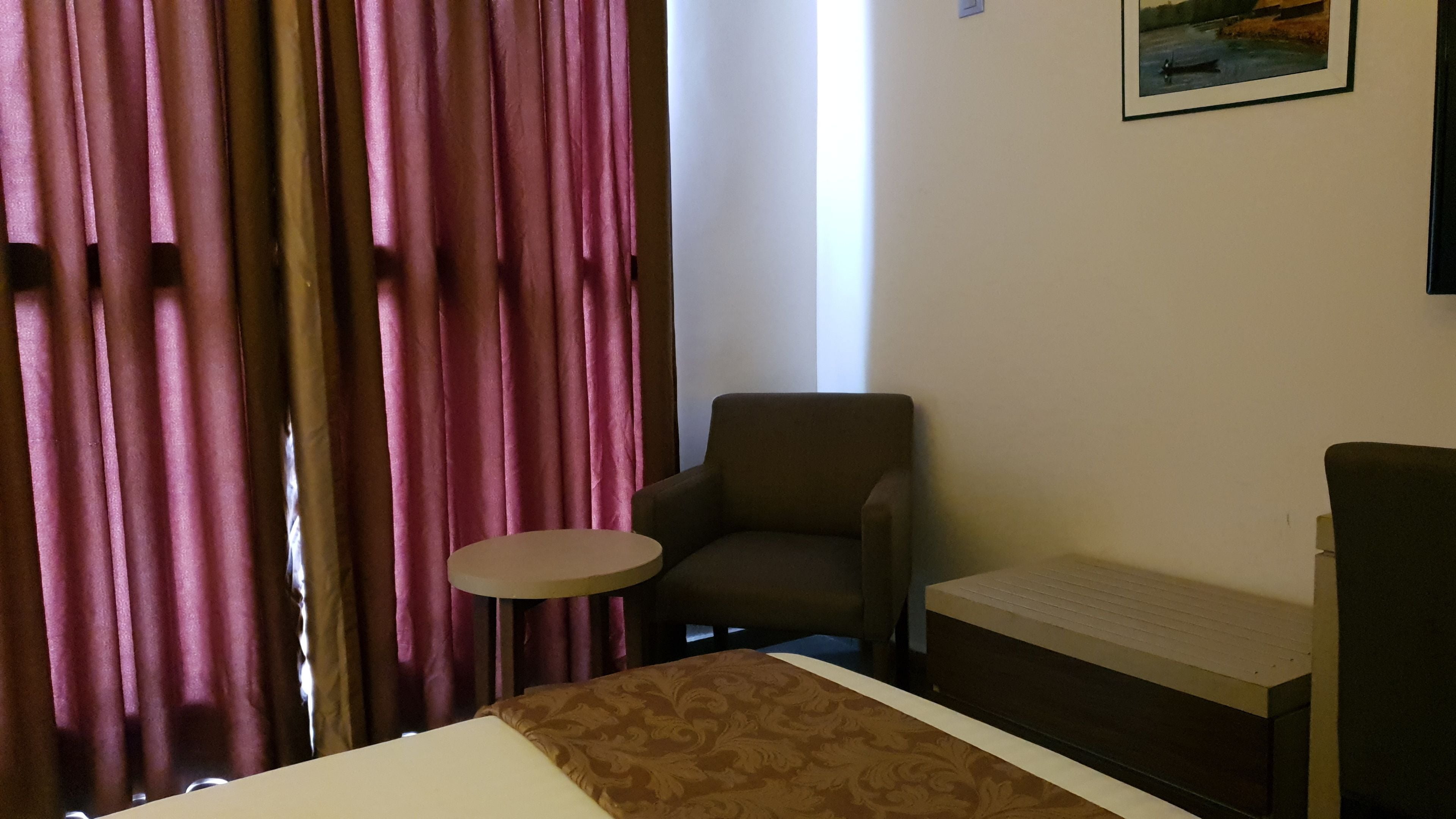 Una habitación de hotel con una cama, una mesita redonda pequeña, un sillón marrón y un sofá.
