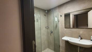 A modern bathroom with a glass-enclosed shower, a sink with a mirror, and beige tiled walls.
