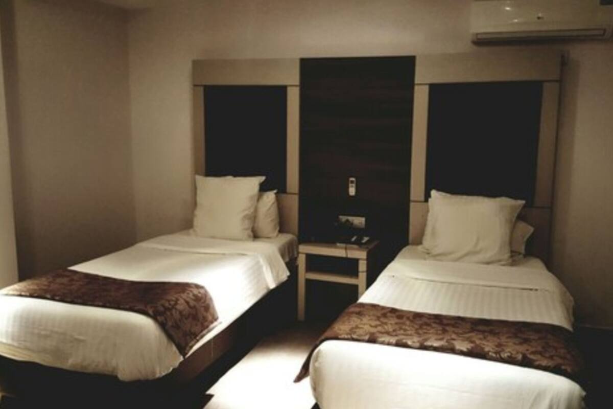A hotel room with two single beds, a small bedside table, and an air conditioning unit above the beds.