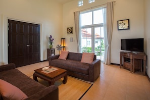 A living room with a sofa, a coffee table, a TV stand, and a large window with curtains.