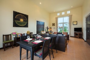 A dining area with a table set for four, surrounded by wicker chairs, a sofa, and a television.