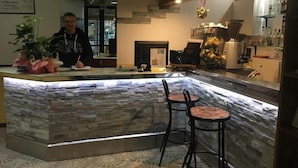 A reception area with a stone counter, two bar stools, a potted plant, and a Christmas tree. - Hotel Adler (Rimini)