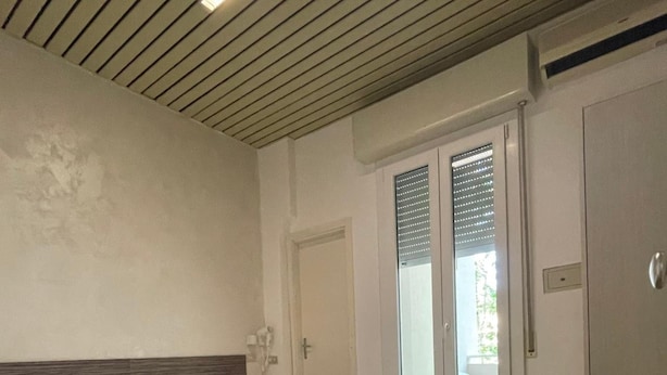 A hotel room with a bed, a chair, a desk, and a sliding glass door leading to an outdoor area. - Hotel Adler (Rimini)