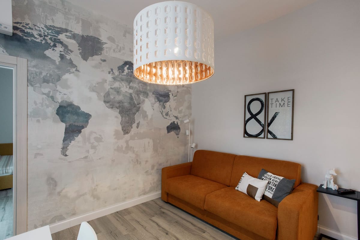 A living room with a world map mural, a white pendant light, an orange sofa, and a framed artwork with the text "8K".