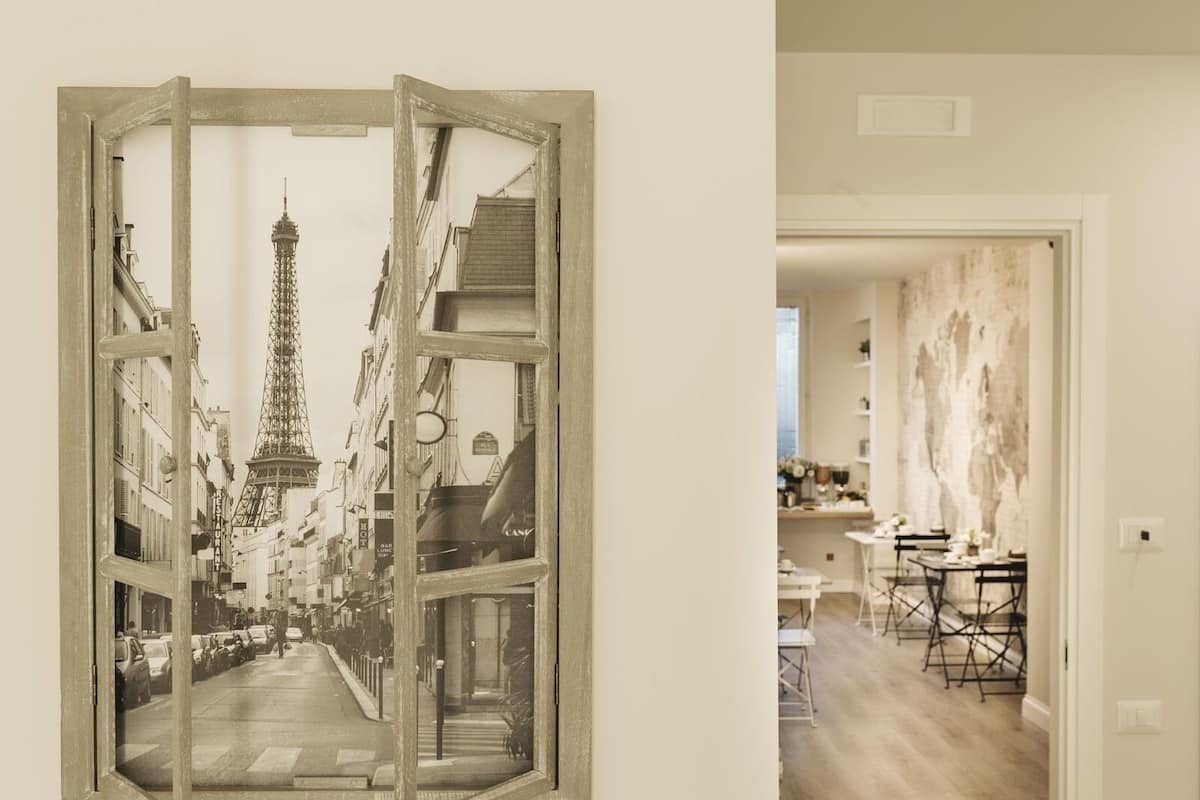 A room with a large window displaying a street view, a dining area with tables and chairs, and a wall with a textured mural.