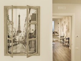 A room with a large window displaying a street view, a dining area with tables and chairs, and a wall with a textured mural.