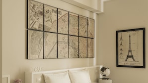 Un dormitorio con un gran mapa de París, una ilustración enmarco de la Torre Eiffel, un globo terráqueo sobre una mesita de noche y un letrero con la palabra 'LOVE' en la cabecera.