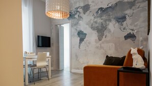 Una sala de estar moderna con un mural de un mapa mundial, una zona de comedor con una mesa y sillas blancas, y un televisor grande en la pared.