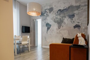 A modern living room with a world map mural, a dining area with a white table and chairs, and a large TV on the wall.