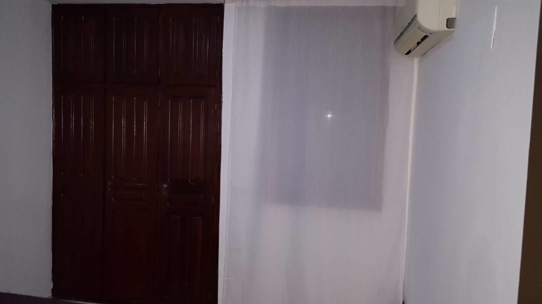 Una habitación con una puerta de madera oscura, una cortina blanca y un equipo de aire acondicionado instalado en la pared.