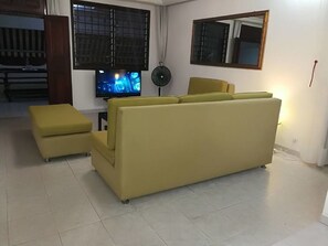 A living room with a yellow sofa, a television, and a fan. - Residence Angele (Abidjan)