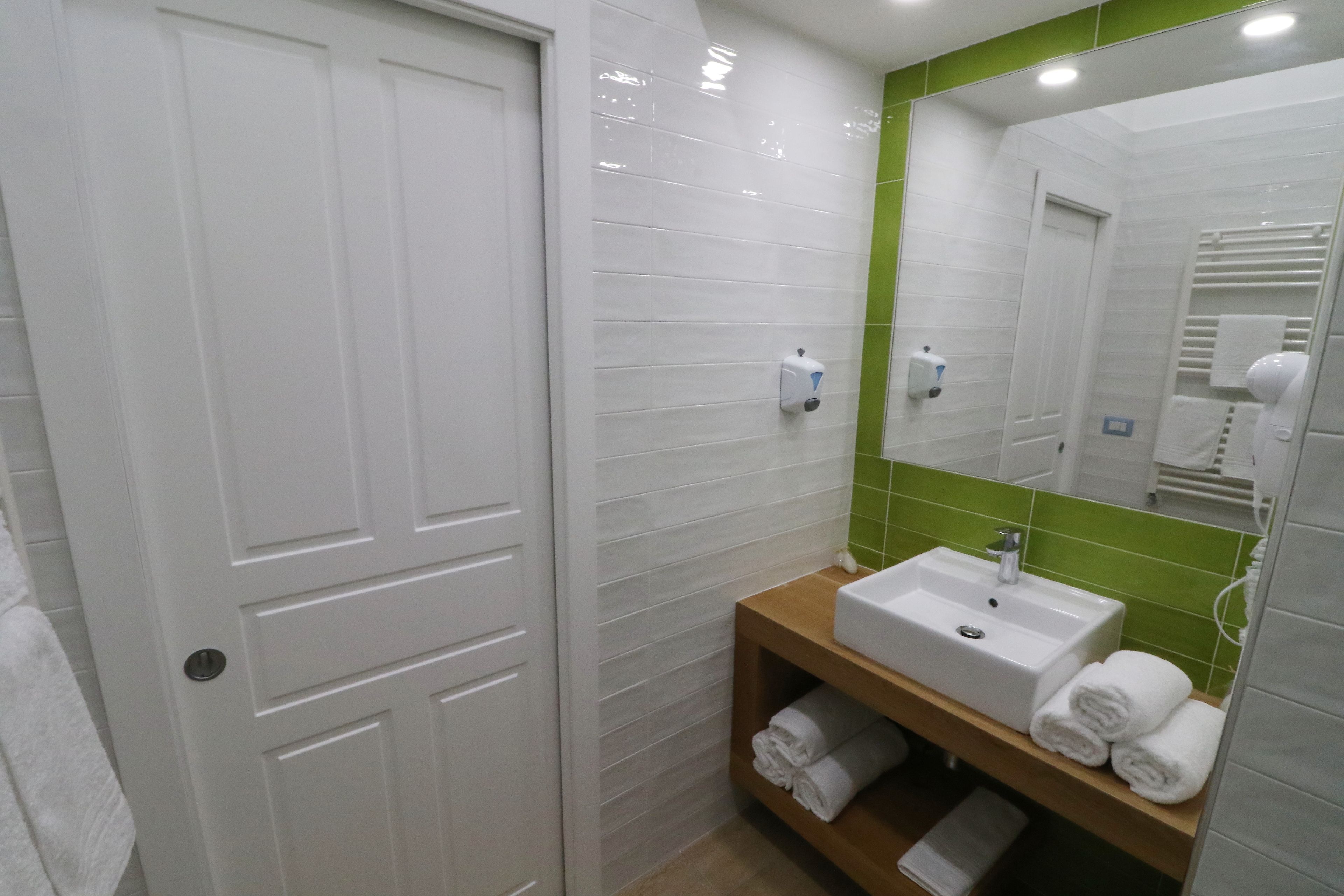 A bathroom with a white door, a sink with a mirror, and green tiles.