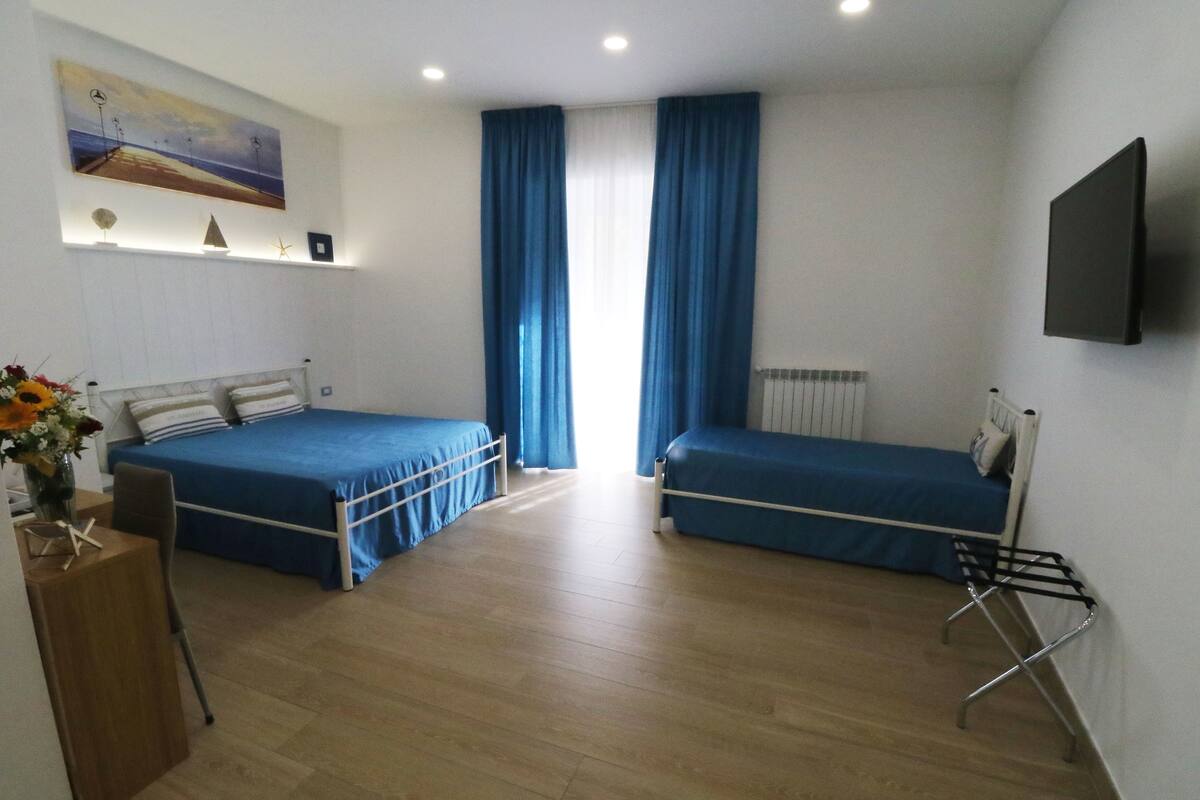 A room with two beds, a desk, a chair, a radiator, and a TV mounted on the wall.