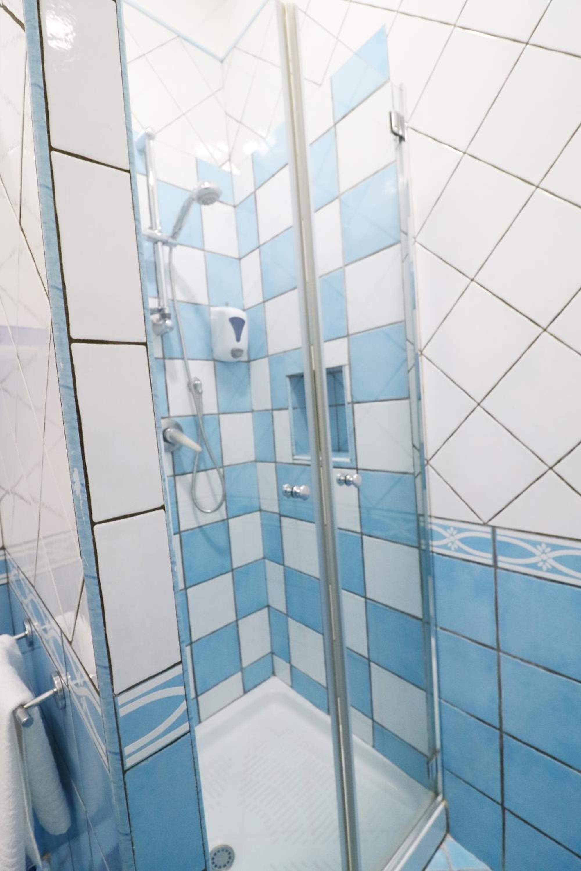 Bagno con cabina doccia in vetro, piastrelle bianche e azzurre e un porta asciugamani a vista.