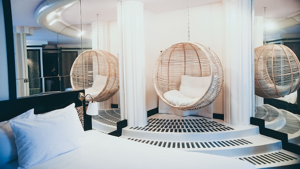 Una habitación de hotel moderna con una cama grande, dos sillones colgantes de mimbre y un diseño de techo circular único.