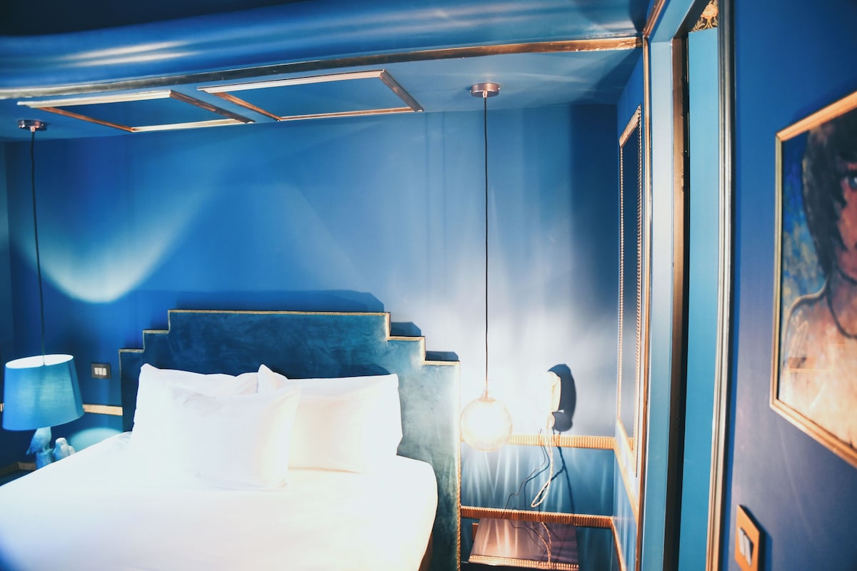 Una habitación de hotel con una cama, una mesita de noche, una lámpara y un cuadro enmarcado en la pared.