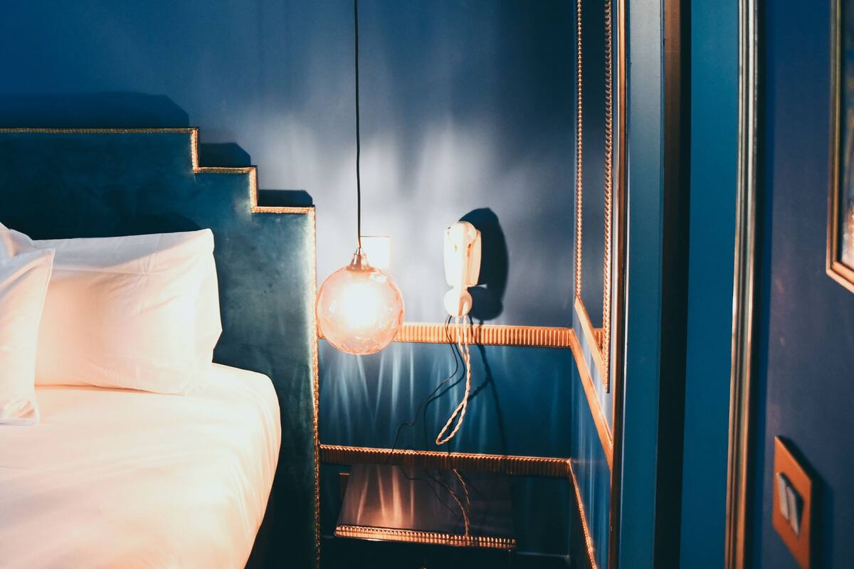 A room with a bed, a hanging light fixture, and a mirror on the wall.