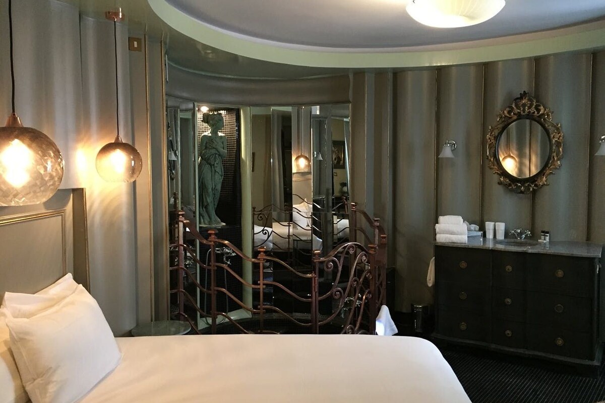 A hotel room with a large bed, a dresser, a mirror, and a staircase leading to a balcony.