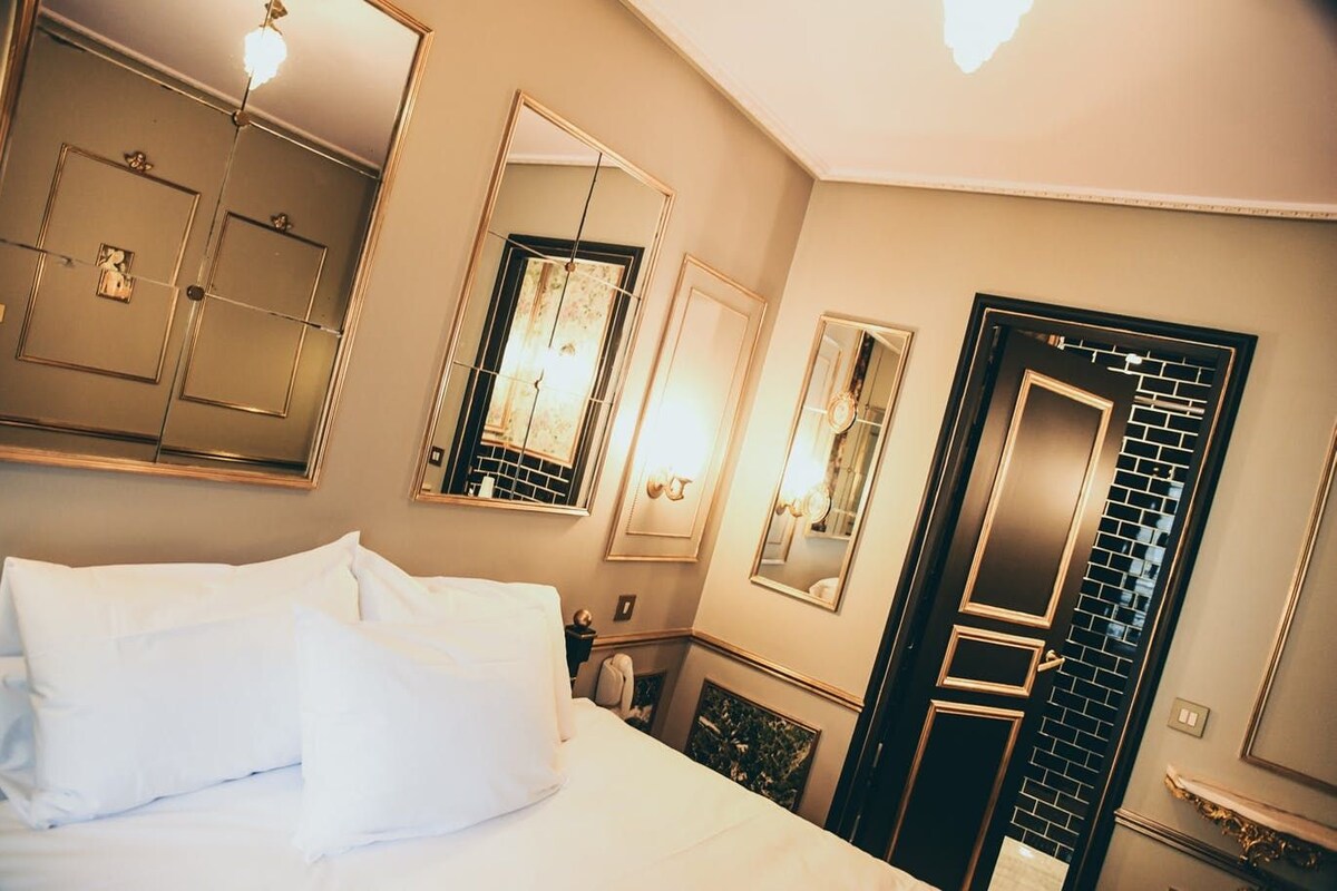 A hotel room with a bed, multiple mirrors, and a door with a black and white pattern.
